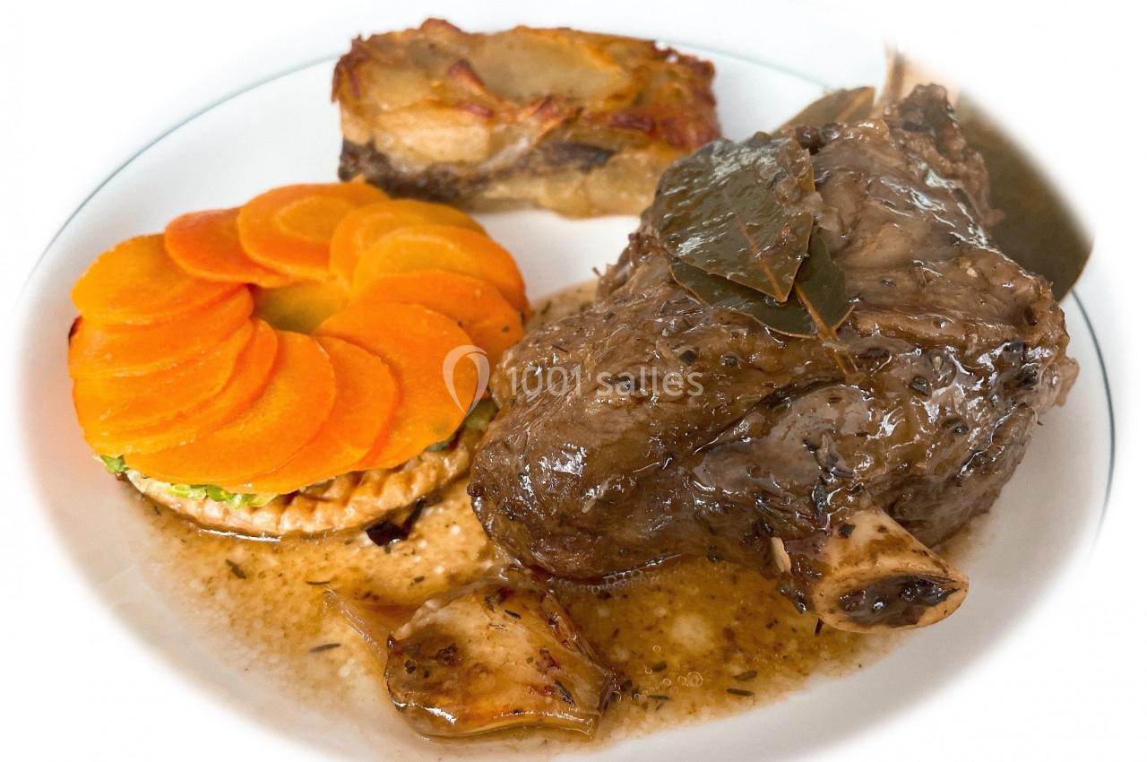 Assiette composée d'un jarret de viande en sauce, d'une garniture de carottes en rondelles et d'un gratin de pommes de terre.