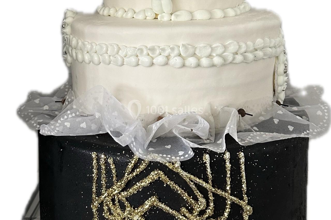Gâteau à trois étages décoré de motifs dorés, plumes blanches et perles, avec une inscription d'anniversaire.