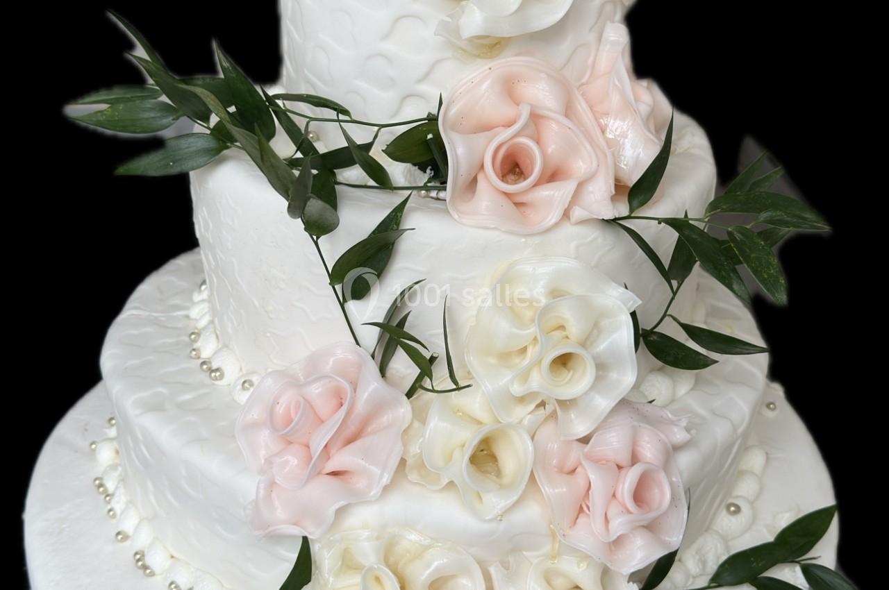 Gâteau de mariage à trois étages décoré de fleurs en sucre roses et blanches avec des feuilles vertes.