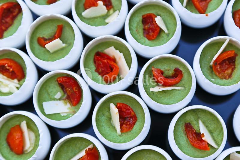 Petits contenants remplis de mousse verte garnie de morceaux de tomate confite et copeaux de fromage.