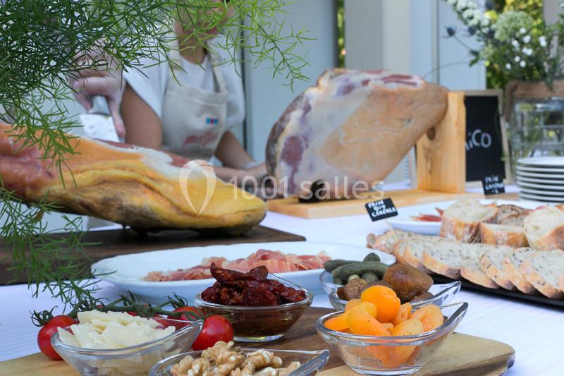 Plateau de charcuterie avec jambon, fruits secs, cornichons, pain et fromages, présenté sur une table en extérieur.