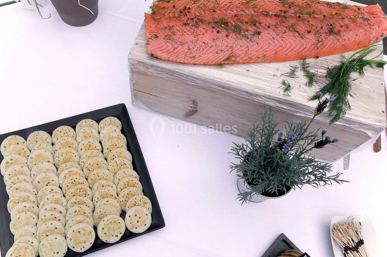 Saumon fumé sur une planche en bois avec des blinis disposés sur une assiette noire, décoré d'herbes fraîches.