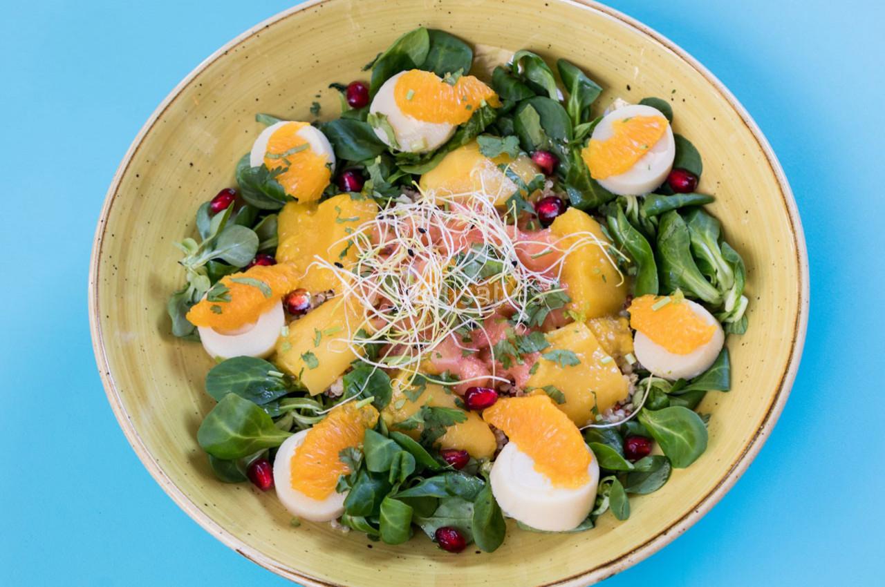 Salade colorée avec mâche, tranches d'orange, graines de grenade, fromage et germes sur une assiette jaune.