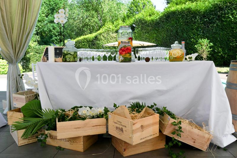 Table décorée avec des boissons infusées, verres alignés, caisses en bois et plantes, en extérieur verdoyant.