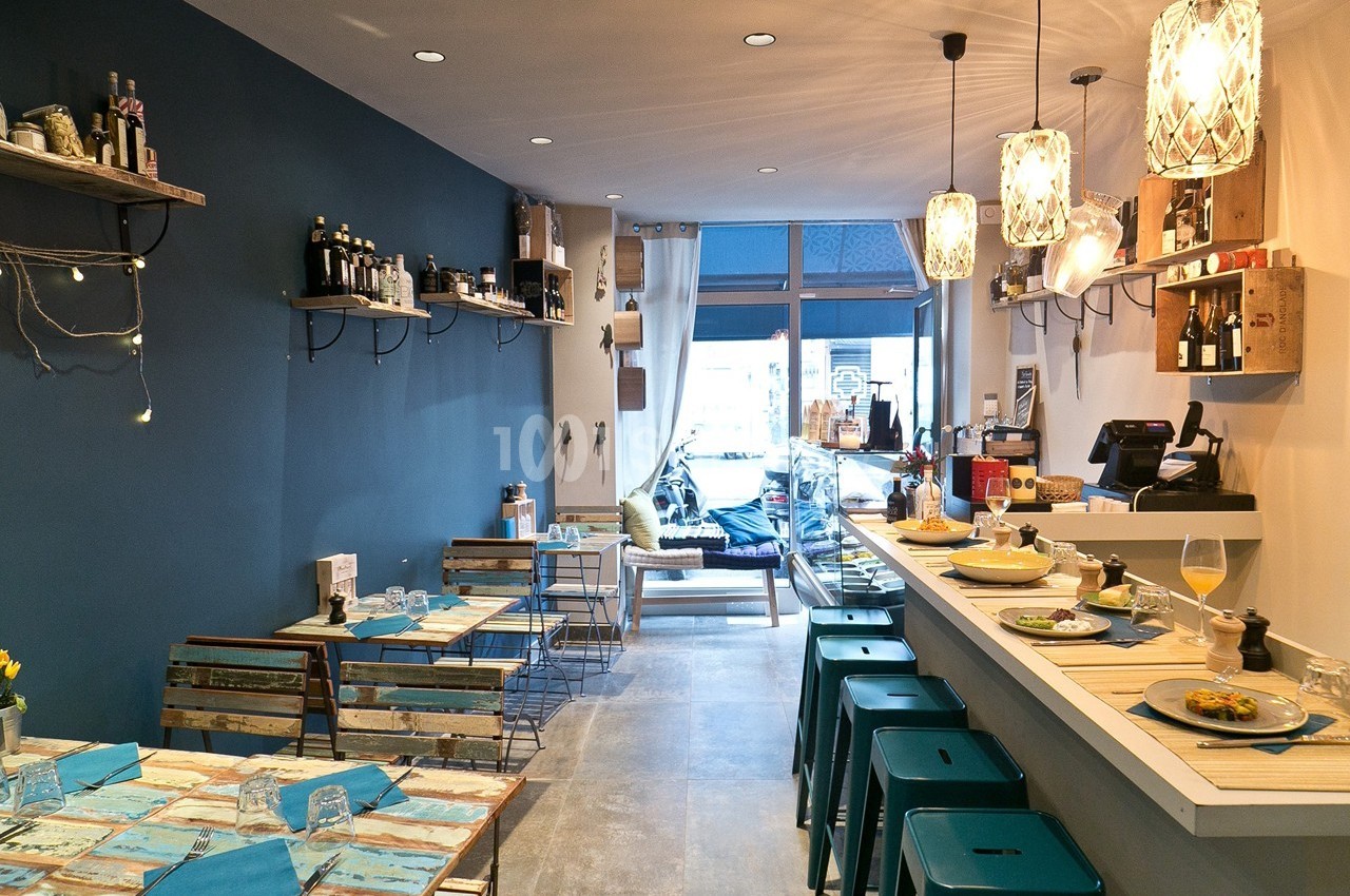 Intérieur d'un café moderne avec tables en bois, tabourets hauts, étagères murales et lumière naturelle provenant de la…