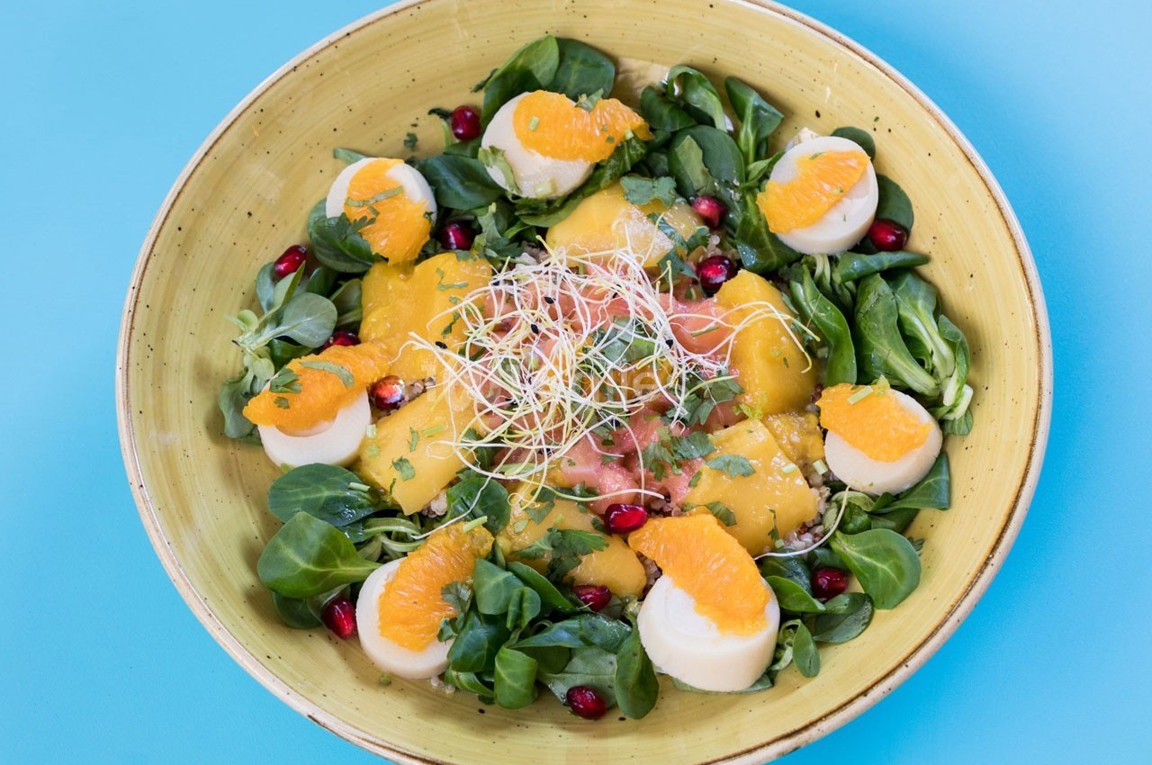 Salade colorée avec mâche, tranches d'orange, fromage, graines de grenade et germes sur une assiette jaune.