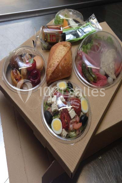 Plateau-repas avec salade, œufs, fromage, pain, légumes, dessert et bouteille de vinaigrette sur une base en carton.