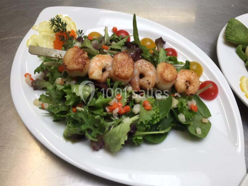 Salade verte garnie de crevettes grillées, tomates cerises et légumes hachés, servie sur une assiette blanche.