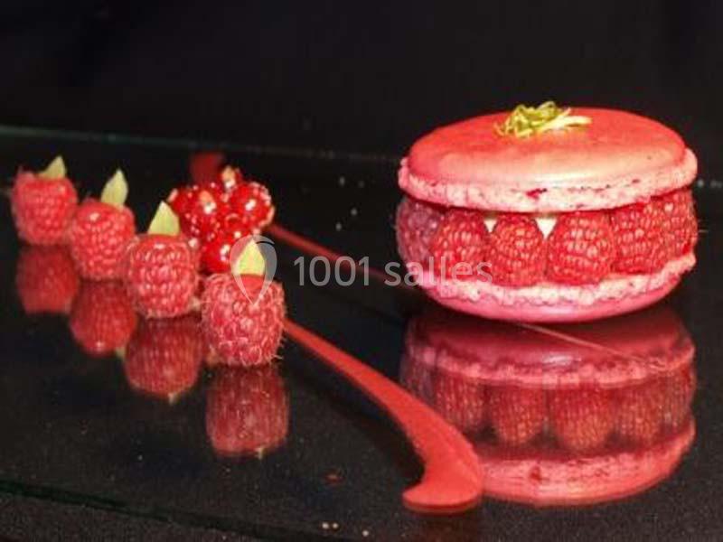 Macaron rose garni de framboises fraîches, accompagné de framboises et groseilles disposées sur une surface noire.