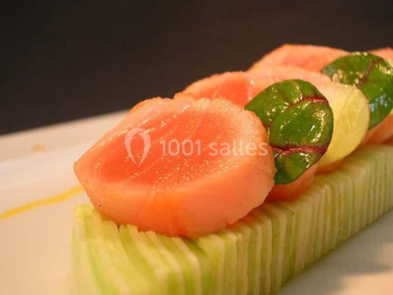 Tranches de saumon cru disposées sur un lit de fines lamelles de concombre, garnies de petites feuilles vertes.