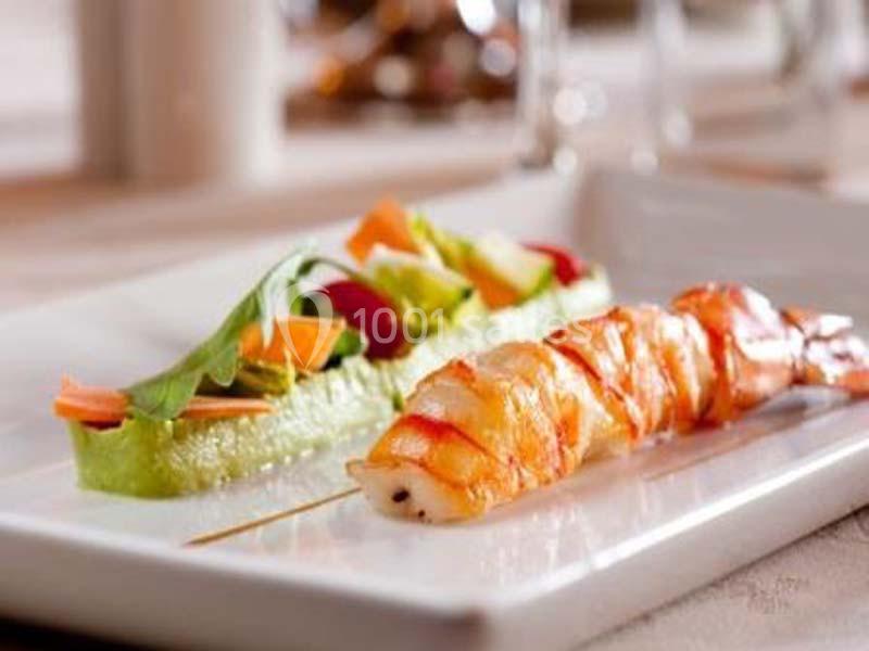 Assiette avec une brochette de crevettes grillées et une garniture de légumes colorés sur un lit de purée verte.