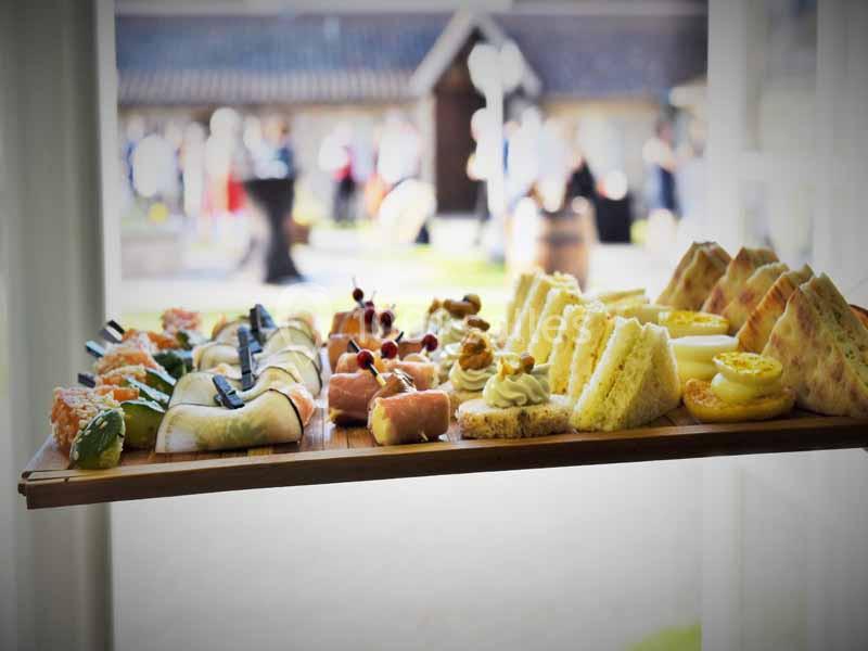 Plateau de bouchées variées comprenant sushis, sandwichs, desserts et amuse-bouches, présenté en extérieur.