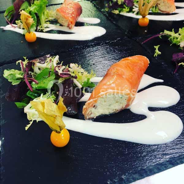 Rouleau de saumon fumé farci, accompagné de salade verte, de physalis et de sauce blanche sur une ardoise noire.