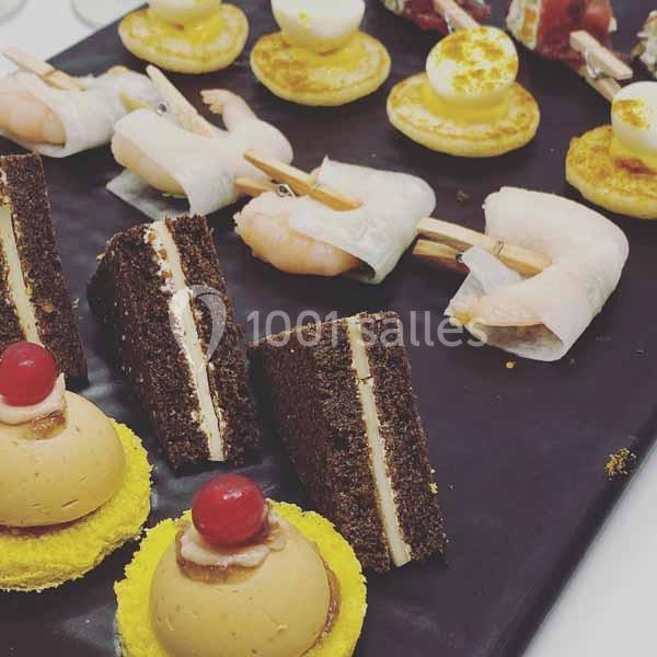 Plateau de bouchées variées comprenant mini-sandwichs, brochettes de crevettes, œufs de caille et desserts colorés.