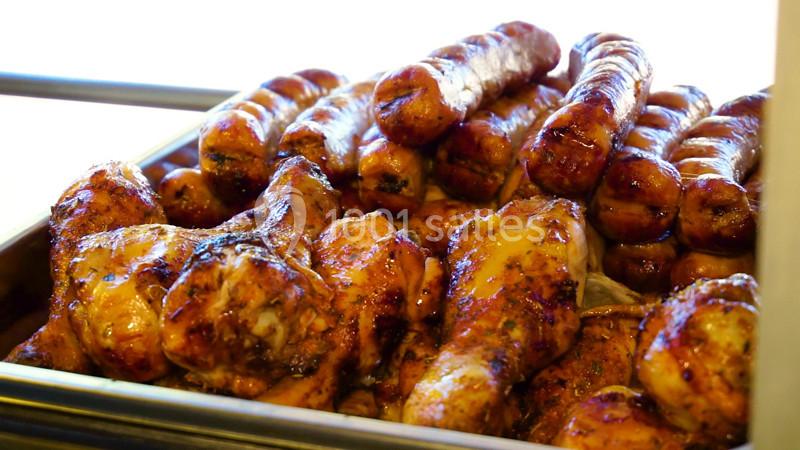 Plateau de saucisses et pilons de poulet grillés, présentés dans un contenant en métal.