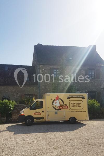 Camion de restauration mobile jaune stationné devant une maison en pierre sous un ciel ensoleillé.
