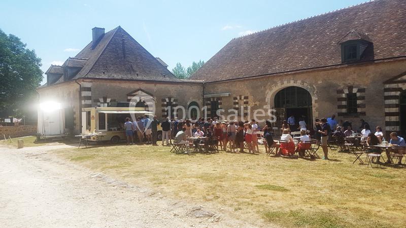 Groupe de personnes rassemblées devant un food truck près d'un bâtiment en pierre, avec des tables en extérieur.