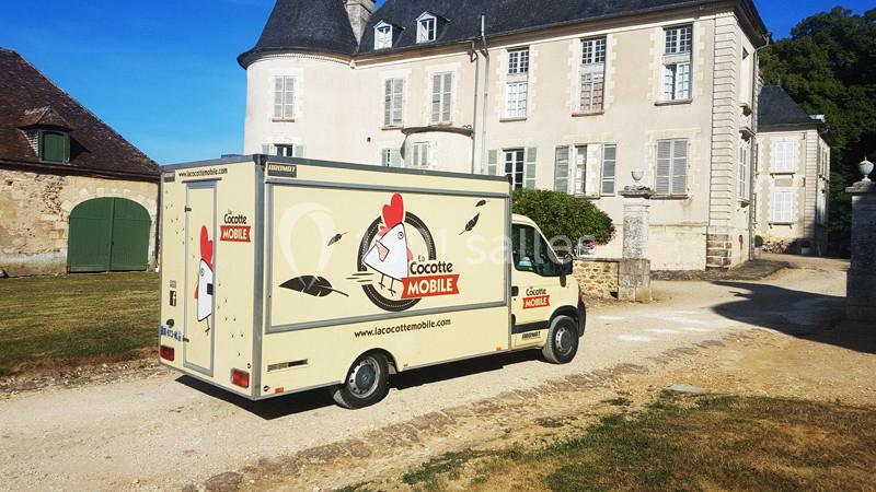 Camion de livraison beige marqué ’La Cocotte Mobile’ stationné devant un bâtiment ancien en pierre.