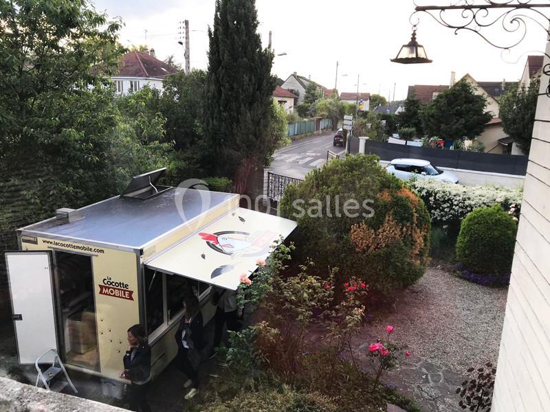 Camion de restauration mobile garé dans une allée résidentielle, entouré de végétation et de maisons.