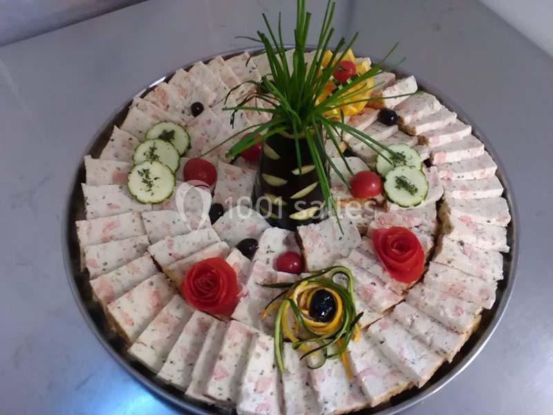 Plateau de charcuterie décorative avec tranches disposées en cercle, garnies de légumes sculptés et herbes fraîches.