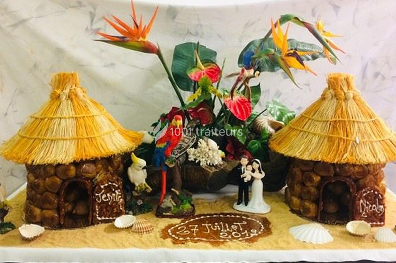 Deux maisons en choux avec toits en paille, décorées de fleurs tropicales, perroquets et figurines de mariage.