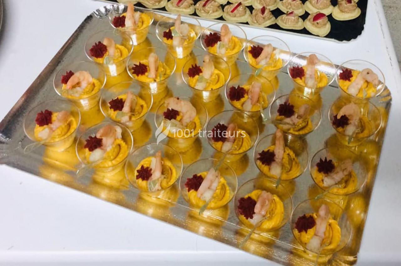 Plateau de verrines contenant une mousse orange garnie de crevettes et d'une décoration rouge, disposées sur une table.