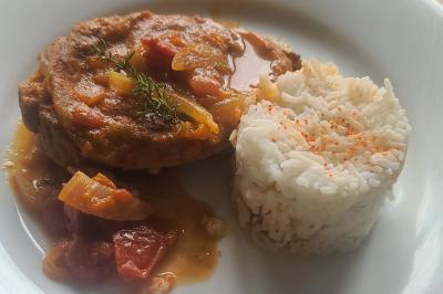 Plat composé d'une cuisse de volaille nappée de sauce, pommes de terre rôties et roulé de légumes en forme de fleur.