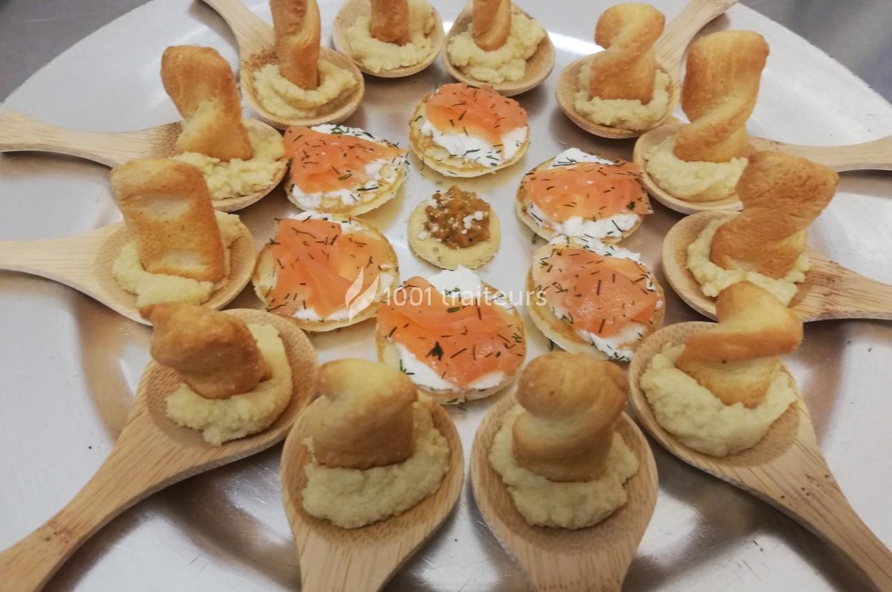 Assortiment d'amuse-bouches sur plateau, avec cuillères en bois garnies et toasts au saumon fumé.