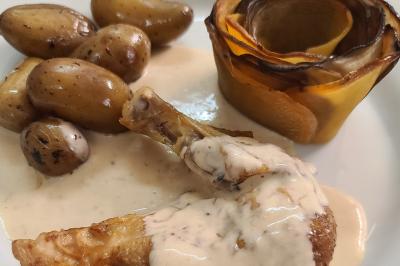 Plat composé d'une cuisse de volaille nappée de sauce, pommes de terre rôties et roulé de légumes en forme de fleur.