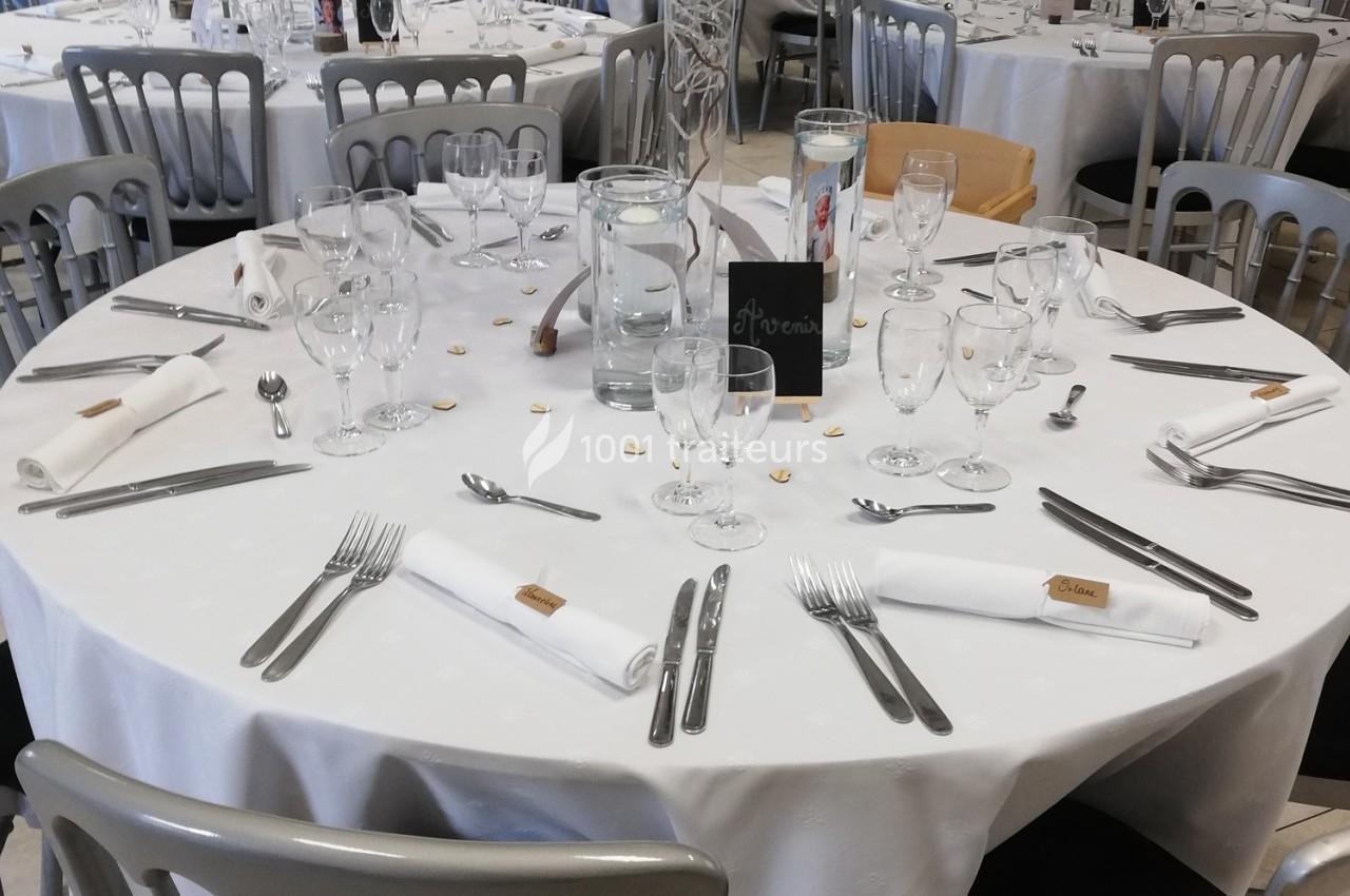 Table ronde dressée avec nappes blanches, couverts, verres, serviettes pliées et décoration sobre pour un événement.