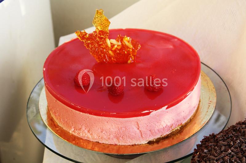 Gâteau rose avec glaçage rouge brillant, décoré de framboises et d'une sculpture en caramel sur le dessus.