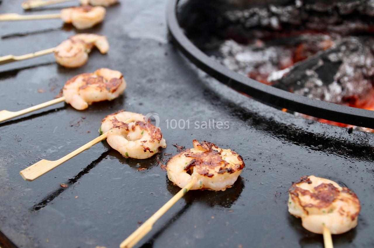 Brochettes de crevettes grillées sur une plaque de cuisson ronde au-dessus de braises.