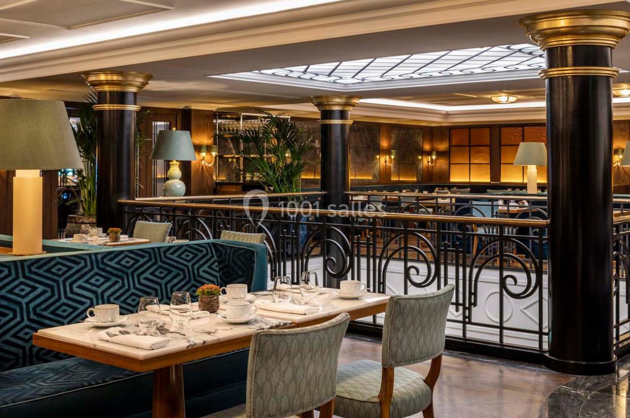 Salle de restaurant élégante avec tables dressées, banquettes en velours bleu et colonnes noires ornées de détails dorés.