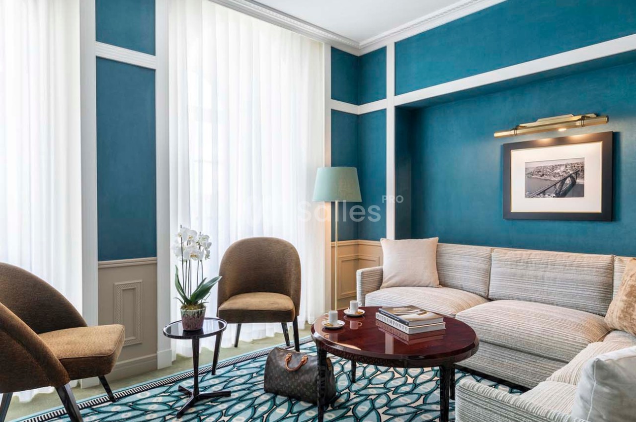 Salon lumineux avec murs bleus, canapé beige, fauteuils, table basse avec orchidée et lampadaire près d'une fenêtre.