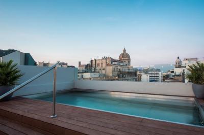 Terrasse en bois avec jacuzzi, deux fauteuils et table, offrant une vue sur un paysage verdoyant.