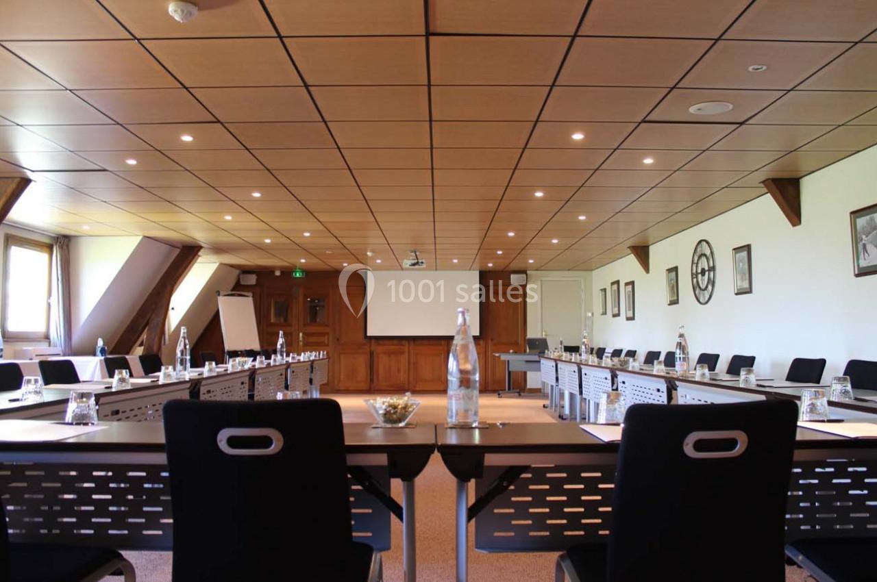 Salle de réunion lumineuse avec tables disposées en U, chaises noires, écran de projection et bouteilles d'eau.