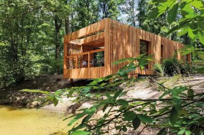 Terrasse en bois avec jacuzzi, deux fauteuils et table, offrant une vue sur un paysage verdoyant.