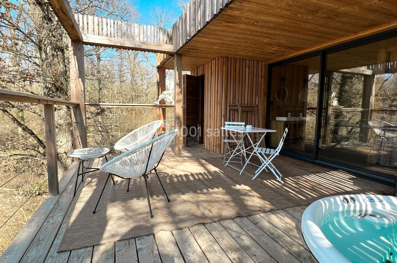 Terrasse en bois avec mobilier d'extérieur, jacuzzi et vue sur une forêt ensoleillée.