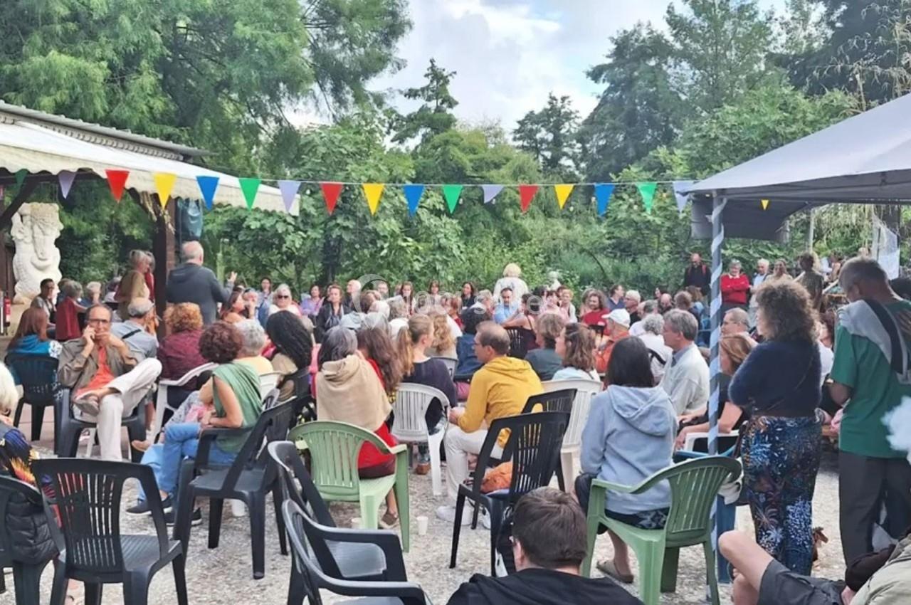 Un groupe de personnes assises en plein air, écoutant un intervenant, entouré de végétation et de guirlandes colorées.