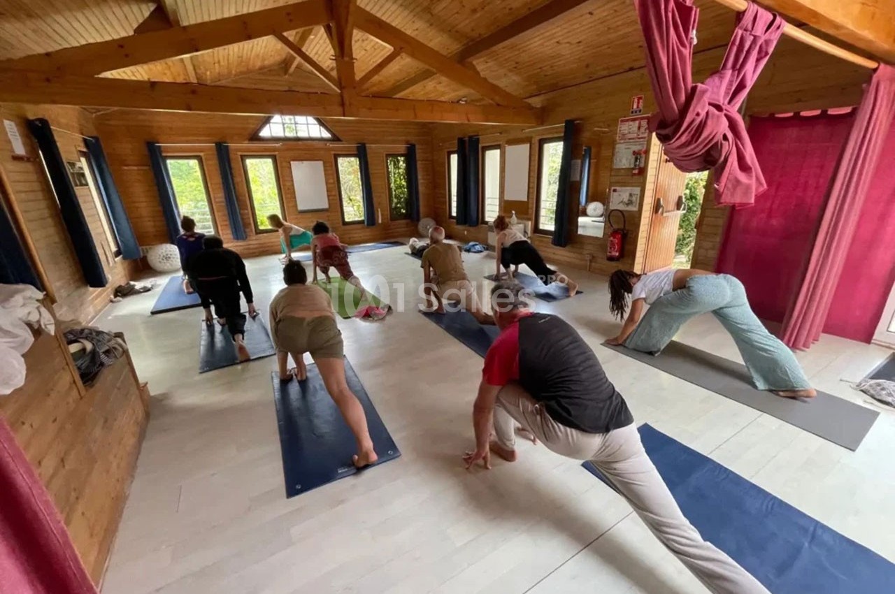 Personnes pratiquant le yoga dans une salle en bois lumineuse, chacune sur un tapis, exécutant une posture d'étirement.