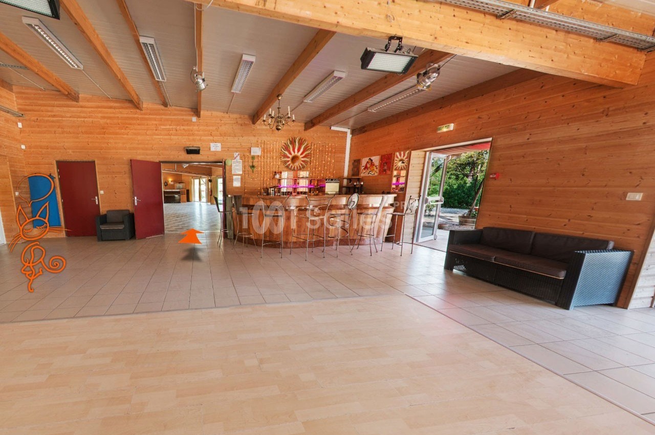 Salle en bois avec un bar central, des chaises hautes, un canapé, et des portes donnant sur un espace extérieur.