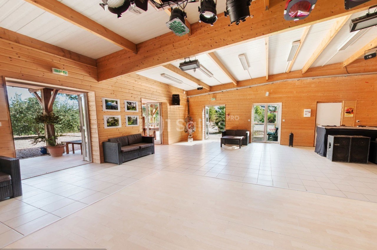 Salle lumineuse avec parquet clair, murs en bois, canapés, baies vitrées donnant sur un extérieur arboré.