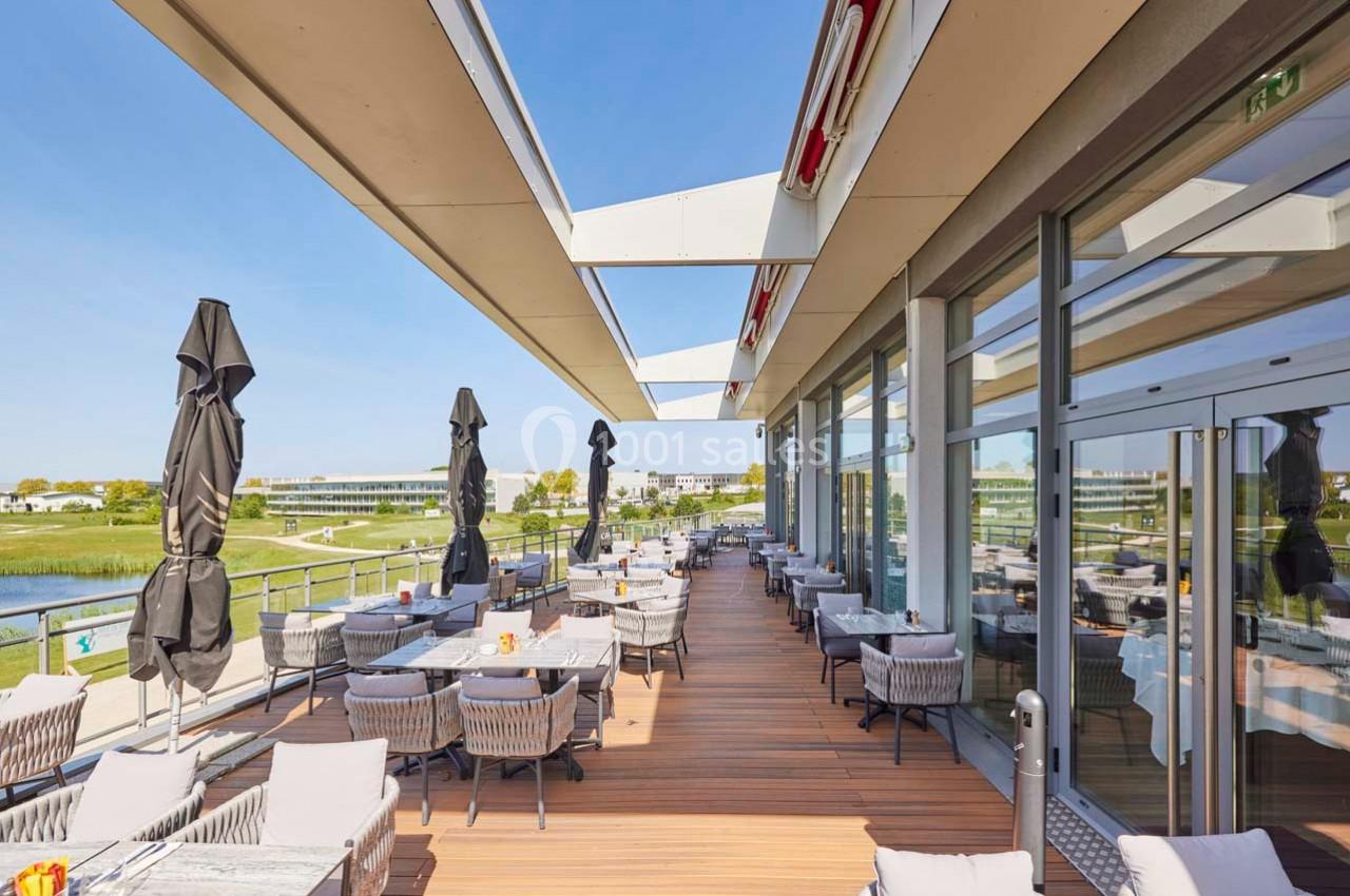 Terrasse extérieure d'un restaurant avec tables, chaises et parasols, offrant une vue sur un paysage verdoyant.
