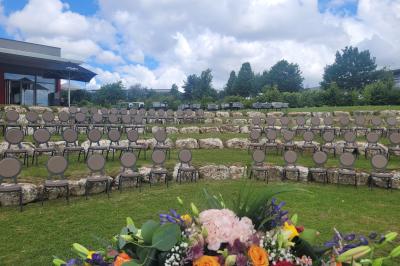 Salle de réception décorée avec des tables dressées, des chaises ornées de nœuds roses et des bouquets de fleurs.