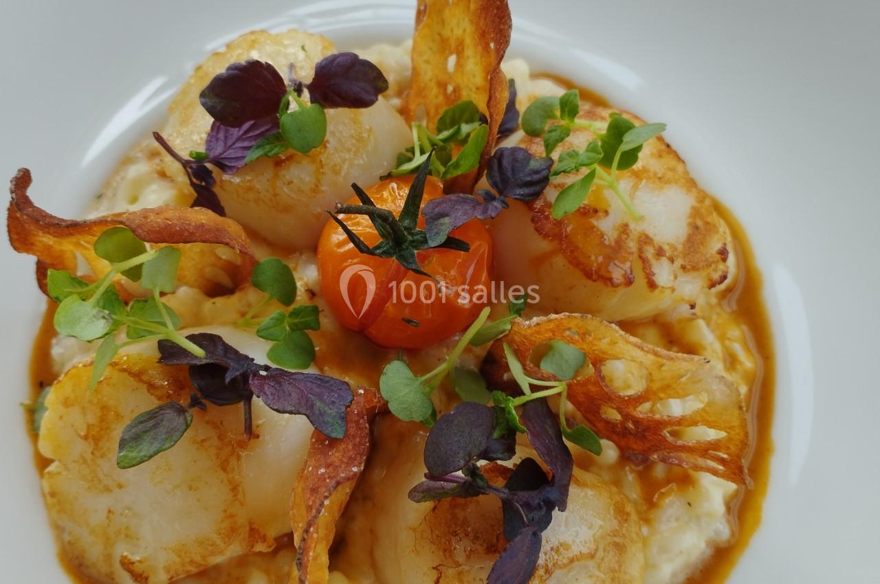 Assiette de noix de Saint-Jacques sur risotto crémeux, garnie de chips croustillantes, herbes fraîches et tomate cerise.