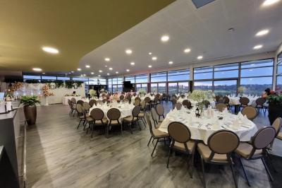 Salle de réception décorée avec des tables dressées, des chaises ornées de nœuds roses et des bouquets de fleurs.
