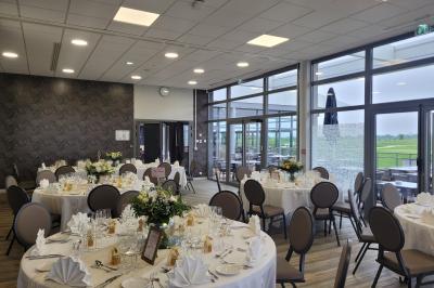 Salle de réception décorée avec des tables dressées, des chaises ornées de nœuds roses et des bouquets de fleurs.