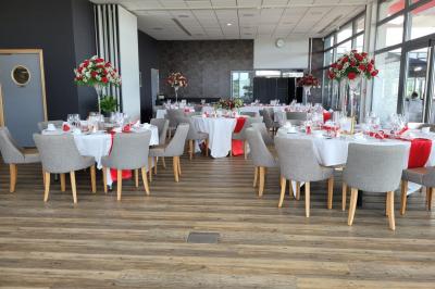 Salle de réception décorée avec des tables dressées, des chaises ornées de nœuds roses et des bouquets de fleurs.