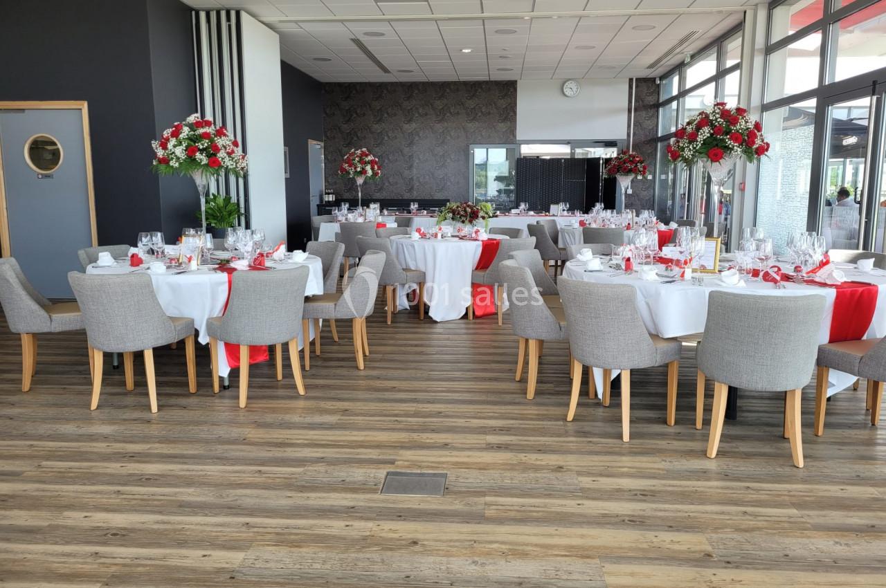 Salle de réception élégamment décorée avec des tables dressées, nappes blanches et accents rouges, chaises grises.