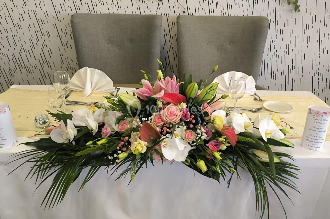 Arrangement floral coloré avec des roses, lys et feuillages, décorant une table blanche dressée pour un événement.